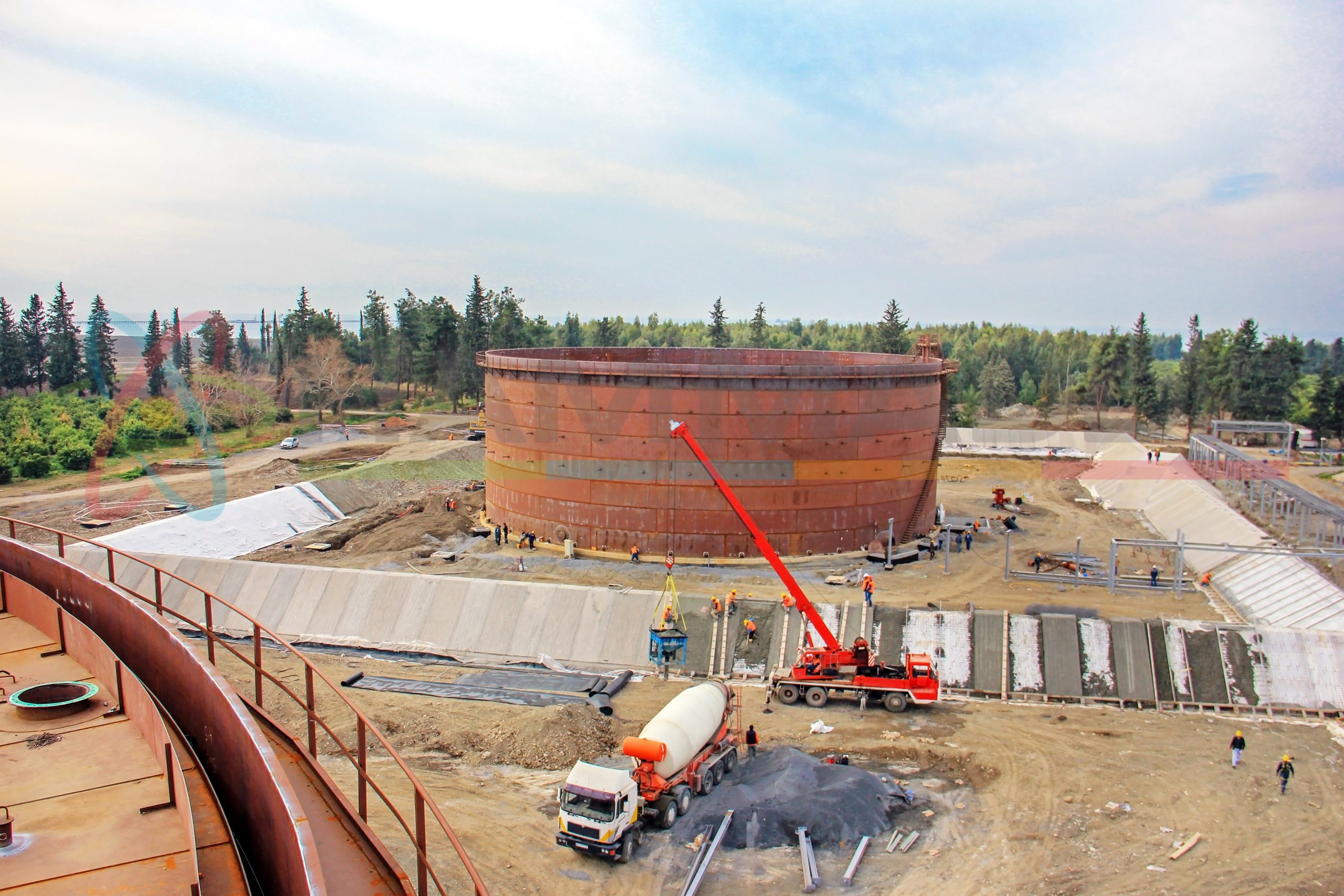 Aerial view of the crude oil storage tanks, a crane, concrete mixer and workers in the construction site. In the USA, storage tanks operate under no (or very little) pressure, distinguishing them from pressure vessels.