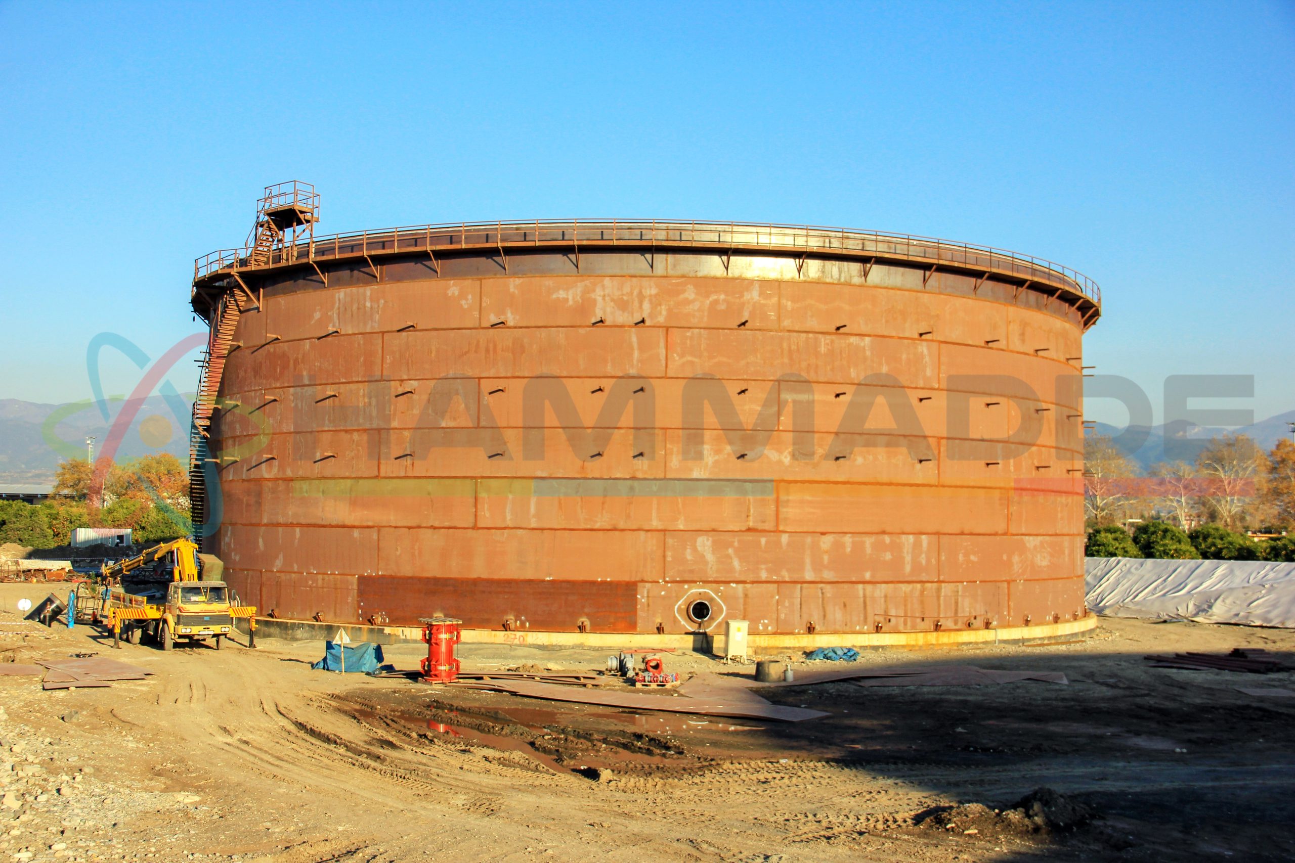 New installation crude oil storage tank with floating roof and a crane in the construction site. Storage tanks are containers that hold liquids, compressed gases or mediums used for the short- or long-term storage of heat or cold.